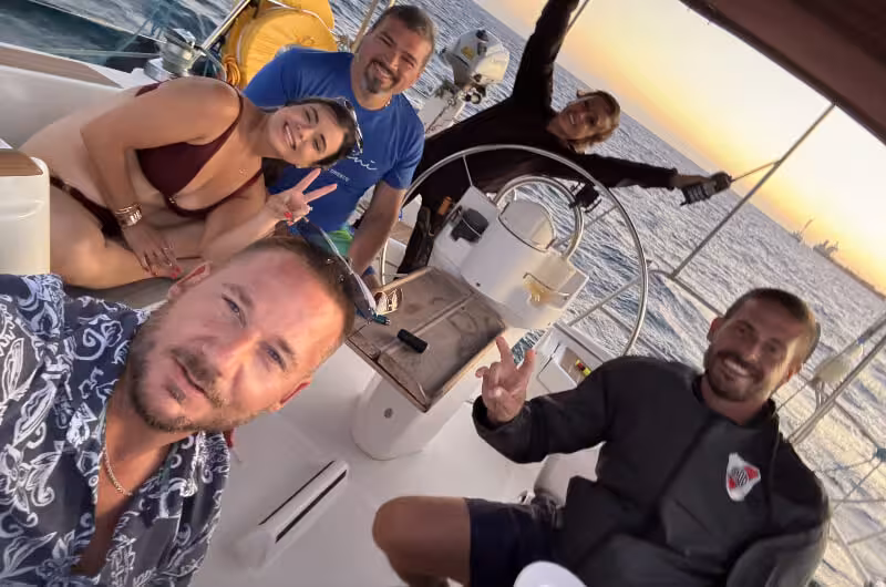 Friends posing on a private Santorini sunset sailing cruise catamaran, enjoying golden hour on the Aegean Sea