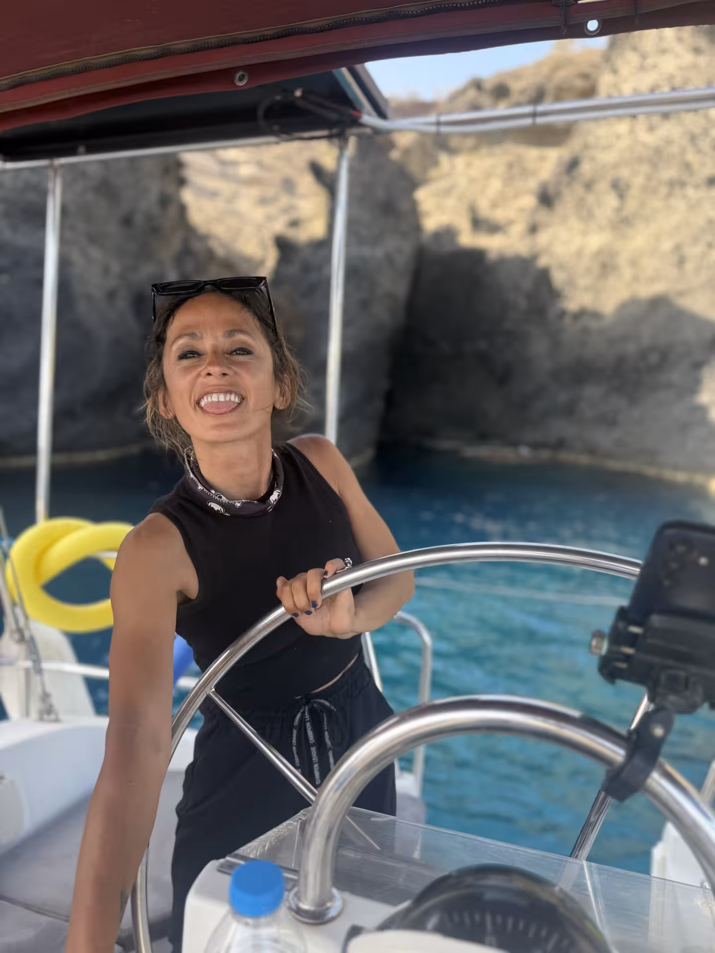 Skipper at the helm on a private Santorini sunset sailing cruise, cruising past volcanic cliffs and blue waters