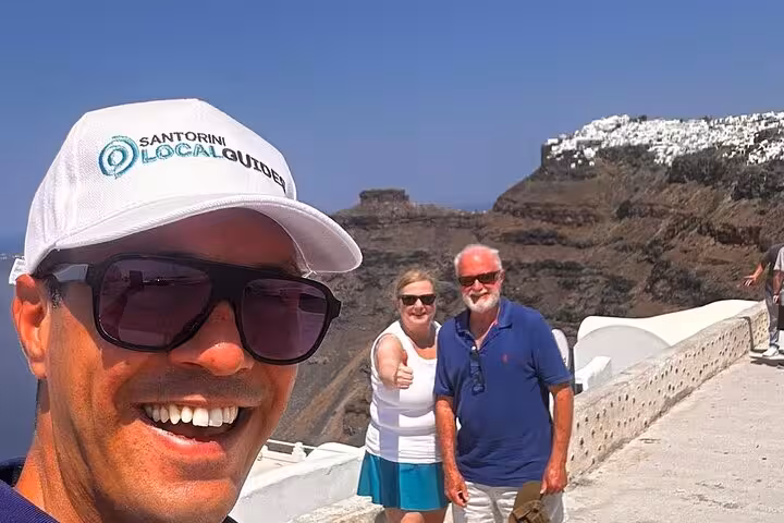 Santorini local guide with travelers at caldera viewpoint during Island of Thera one-day tour and wine tasting
