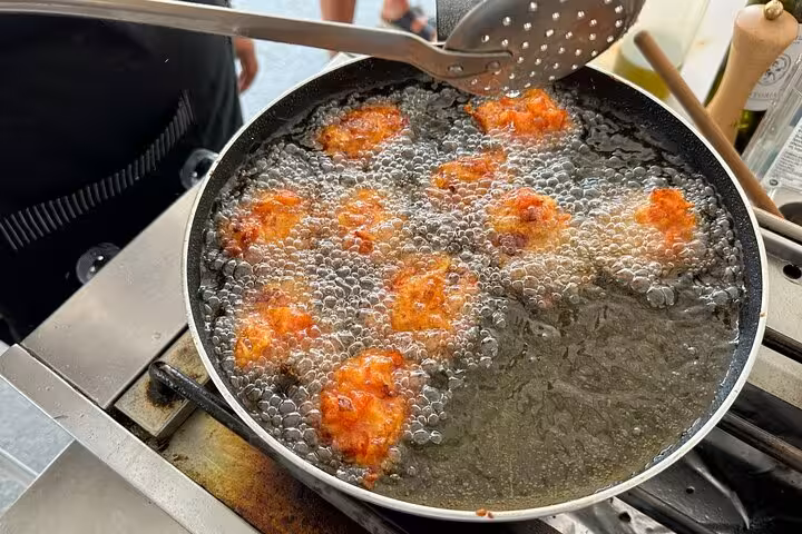 Tomato fritters frying in pan during Santorini private cooking class, traditional Greek meze on island tour experience