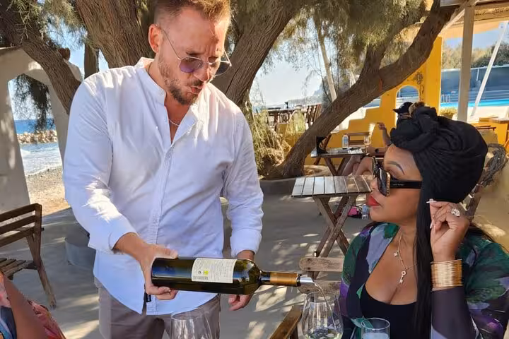 Wine tasting on Santorini private tour from Athens, sommelier pouring Greek wine at seaside taverna