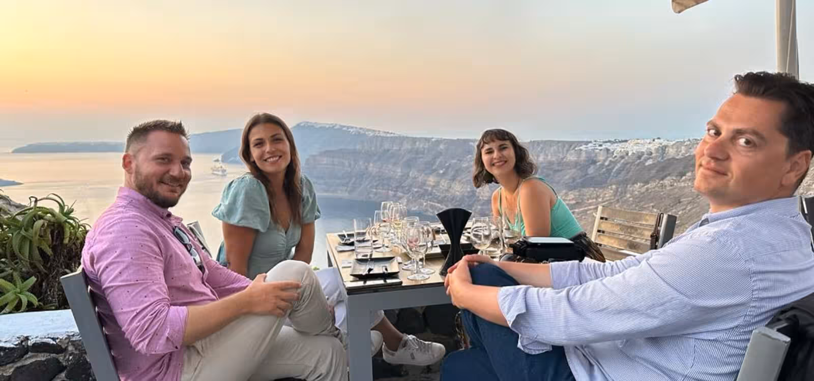 Friends enjoy private Santorini wine tasting at sunset with caldera views, glasses set on terrace table