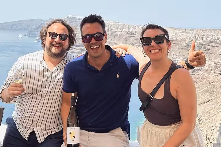 Happy guests with wine bottle on Santorini caldera viewpoint during private wine tasting tour with lunch