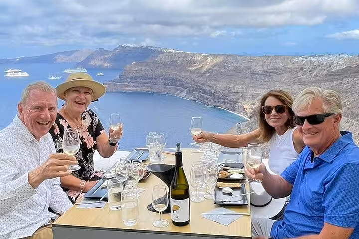 Guests toast with Santorini wine at caldera-view lunch during a private wine tasting tour to 4 wineries