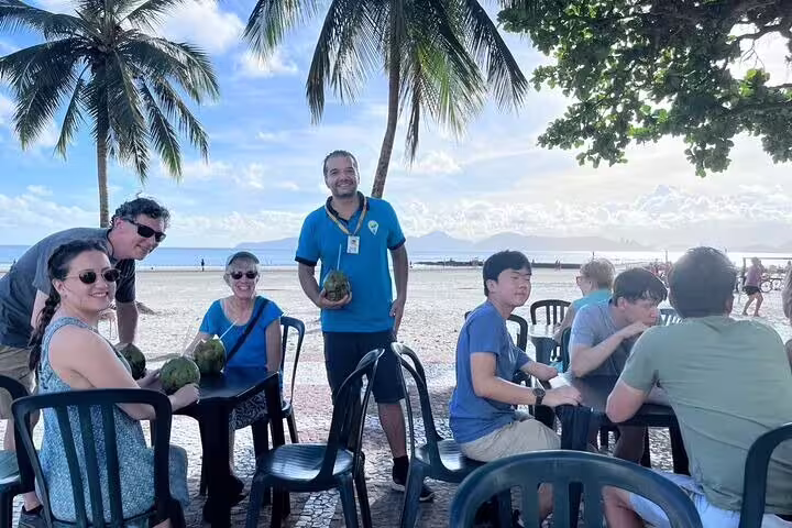 Visitors relaxing under palm trees with coconuts at a beachside cafe on the Santos full-day tour.