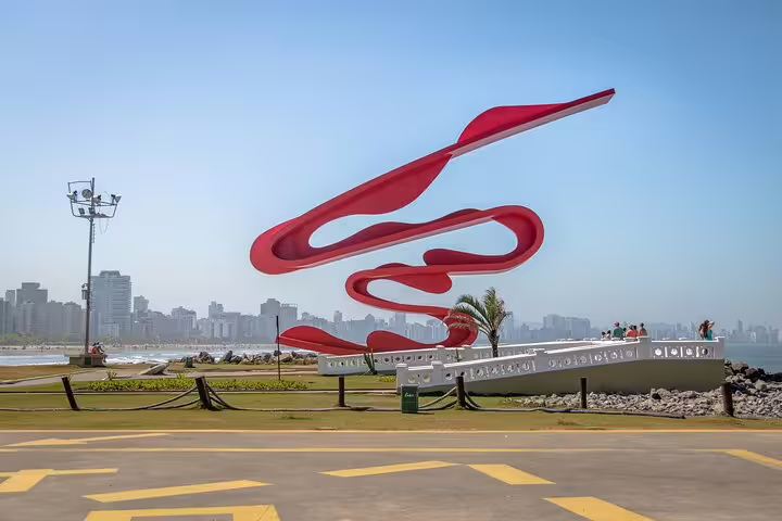 Modern red sculpture on the Santos beachfront with city skyline in the background, a highlight of the sightseeing tour.