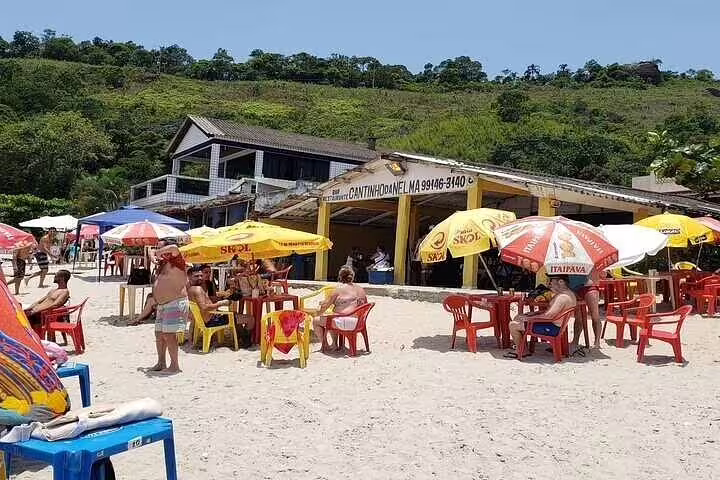 Beachgoers relax under colorful umbrellas at a lively beachside restaurant in Santos, enjoying the summer vibe.
