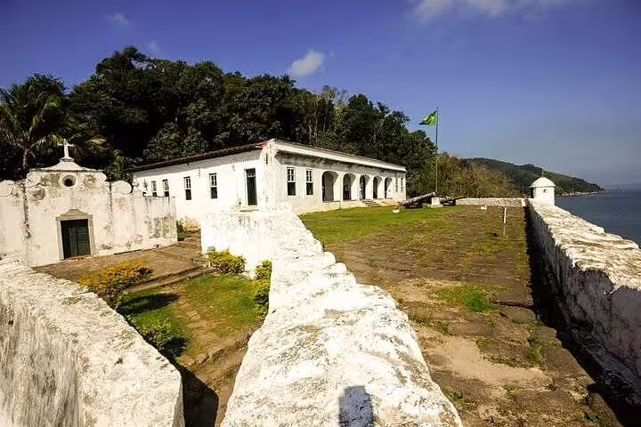 Historic fort in Santos with lush greenery and ocean view, a highlight stop on a private boat tour with barbecue and drinks.