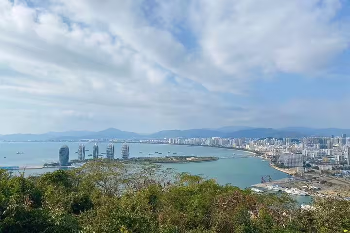 Panoramic view of Sanya Bay with modern skyline and lush greenery from Luhuitou Peninsula vantage point.