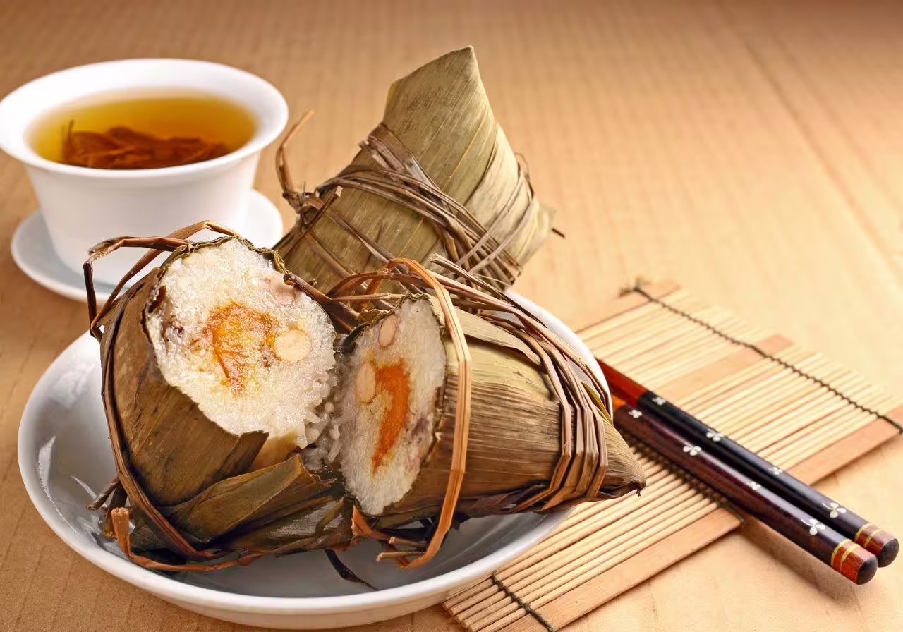Traditional Chinese zongzi rice dumplings on a plate with tea, offering a taste of Sanya's authentic cuisine.