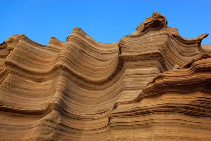 Majestic sandstone waves under a clear blue sky, highlighting Carbeirinho's geological beauty on São Nicolau.