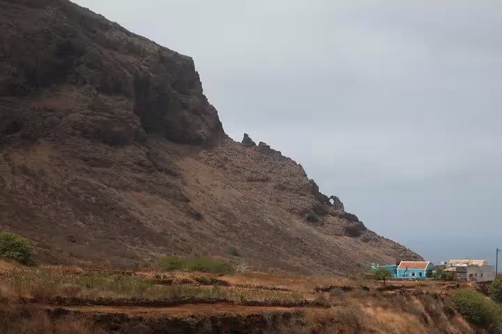 Dramatic rocky cliffs tower over quaint houses in São Nicolau, highlighting the rugged beauty of the hiking trail.