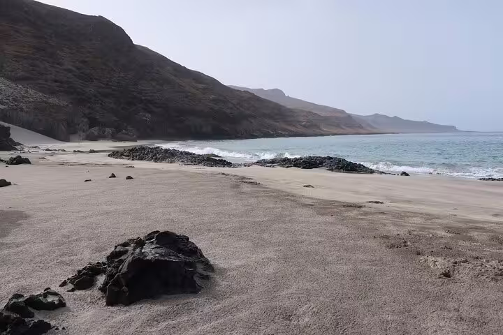 Expansive sandy beach with rugged mountains and azure waters, perfect for hiking in São Nicolau's Tarrafal region.