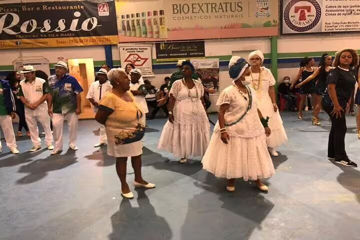 Dancers in white attire perform at a São Paulo samba school, showcasing traditional Brazilian music and dance.
