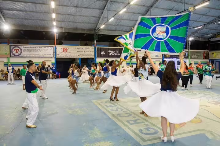 Vibrant São Paulo samba school rehearsal featuring dancers in white skirts and colorful flags under bright lights.