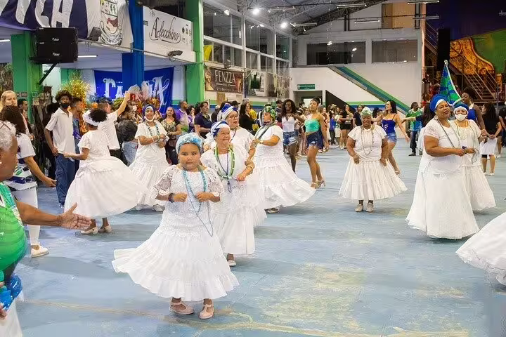 Women in traditional white dresses dance at a São Paulo samba school rehearsal, celebrating Brazilian culture.