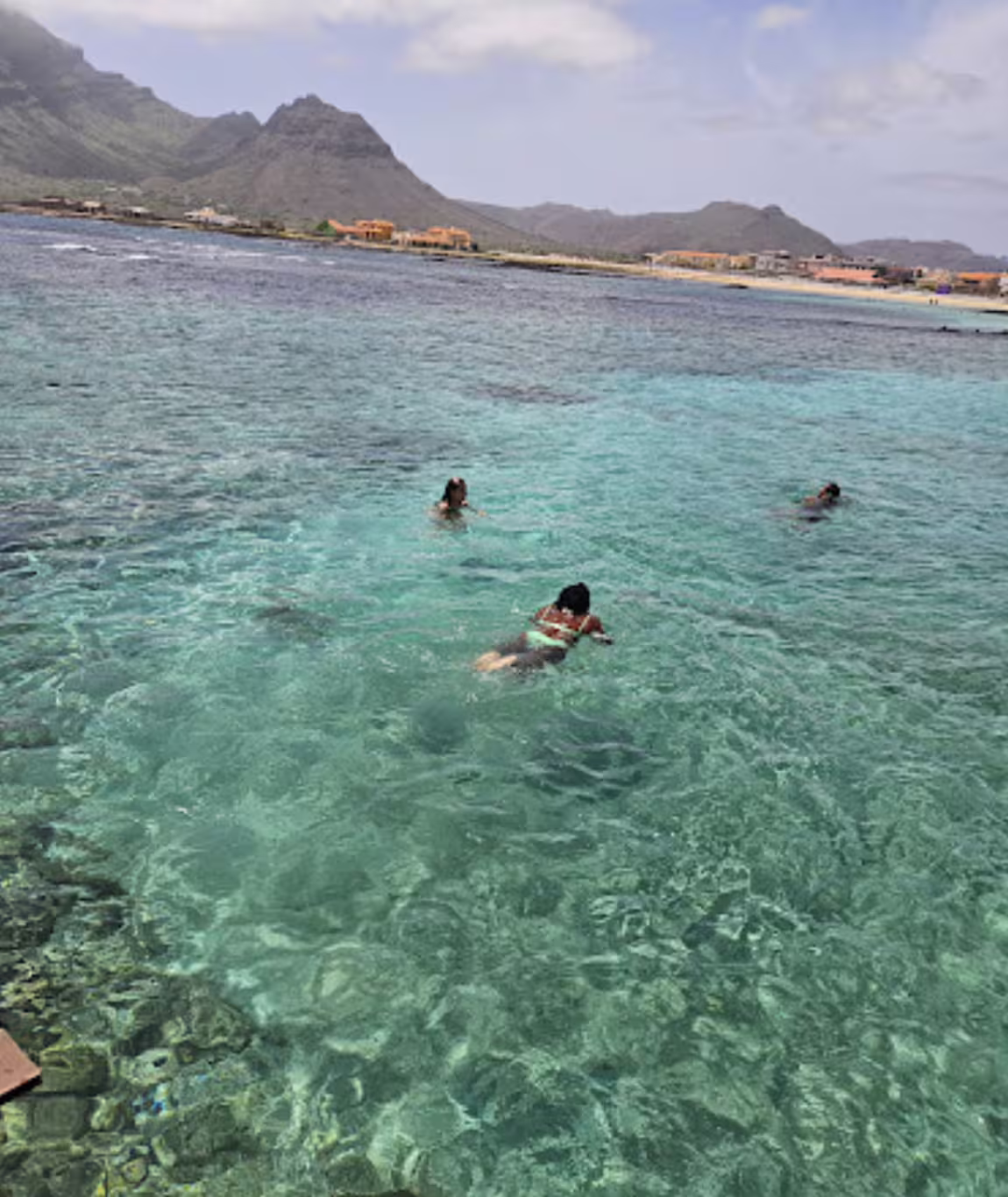 Clear turquoise waters of São Vicente beach with swimmers, surrounded by mountains and villages, ideal for a half-day tour.