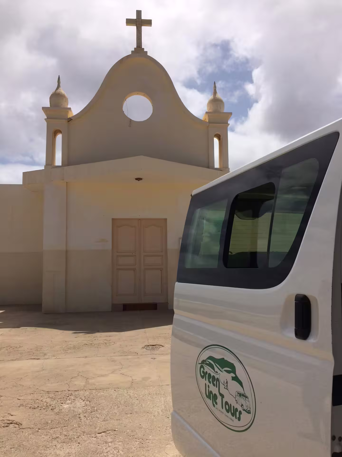 Tour van parked by a historic church under a blue sky in São Vicente, ideal for exploring beaches and Monte Verde.
