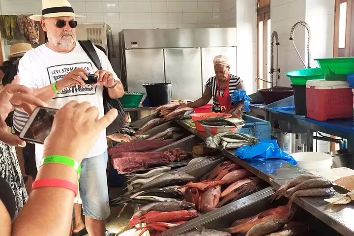 Visitors engage with a local vendor at a bustling São Vicente fish market, showcasing a vibrant display of fresh seafood.