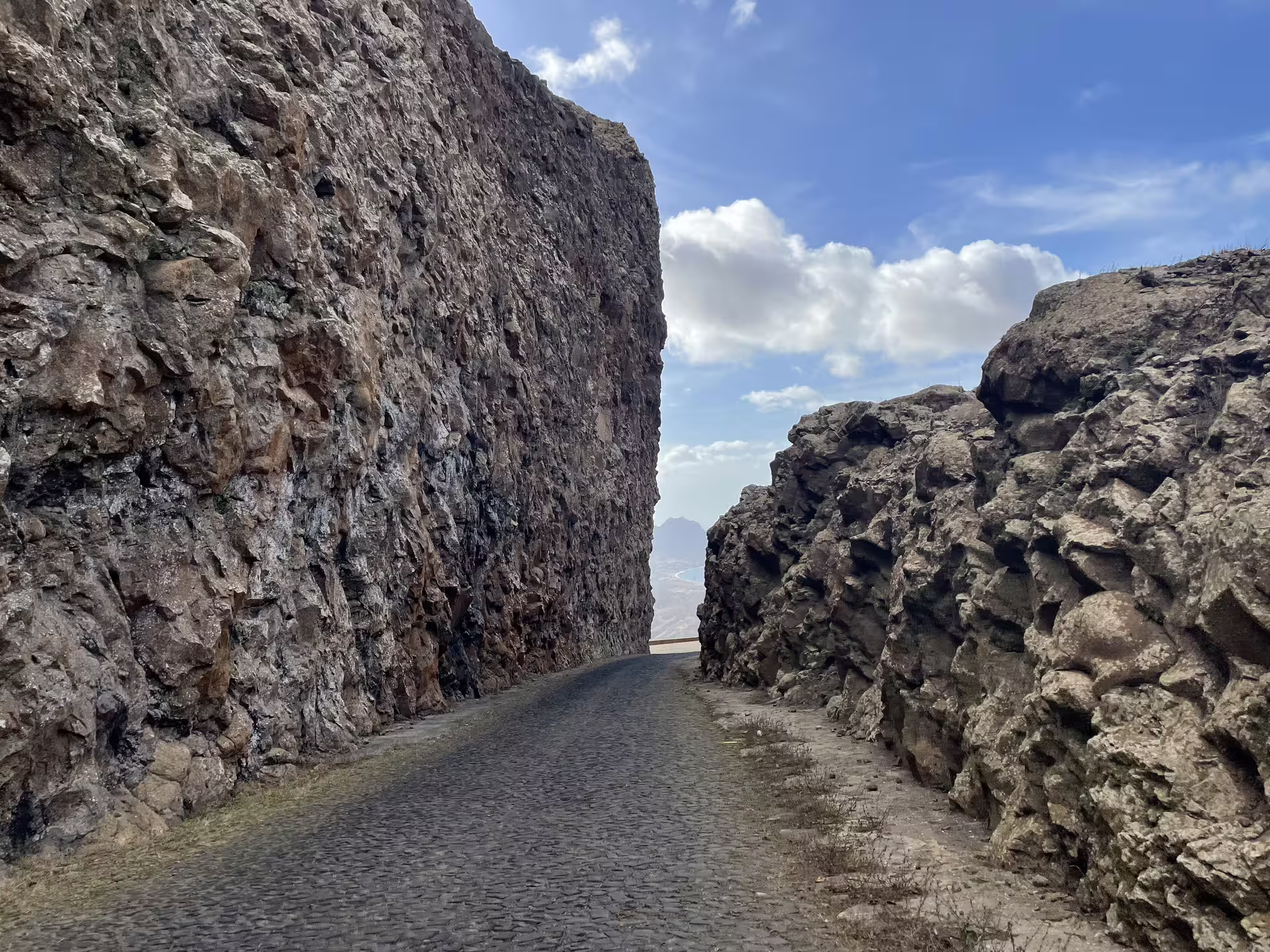 Scenic cobblestone road winding through dramatic rocky cliffs under a bright blue sky on São Vicente's Mindelo tour.