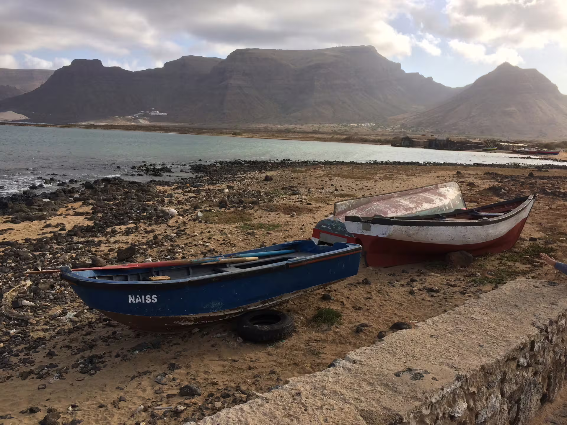 Scenic view of rustic boats on a rocky beach with São Vicente mountains in the background during a Mindelo shore excursion.