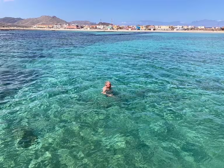 Clear turquoise waters of São Vicente with a distant view of Mindelo's colorful shoreline, perfect for a full-day shore excursion.