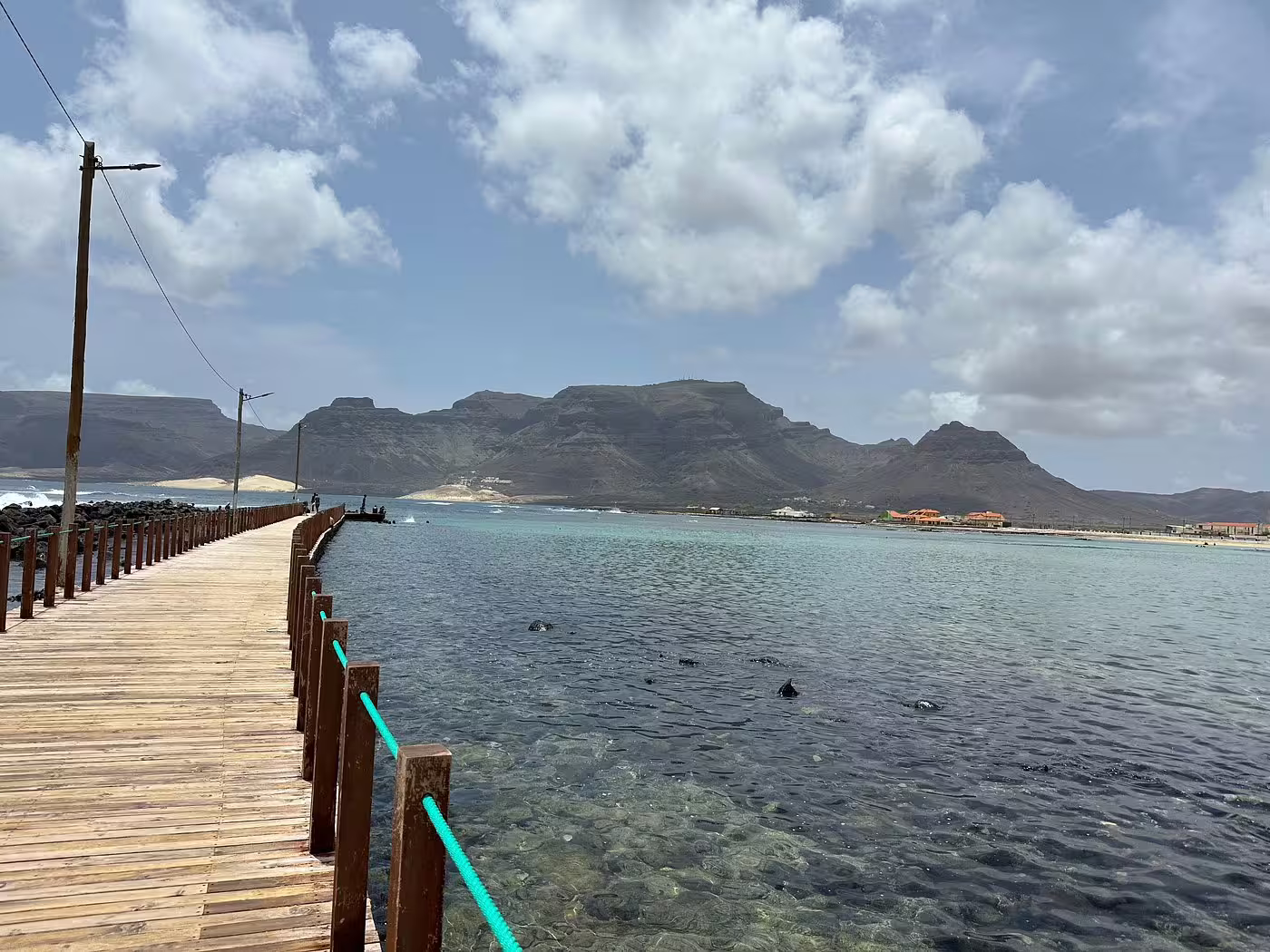 Scenic view of the wooden pier and turquoise waters in São Vicente, Mindelo, with mountainous backdrop on a full-day shore excursion.