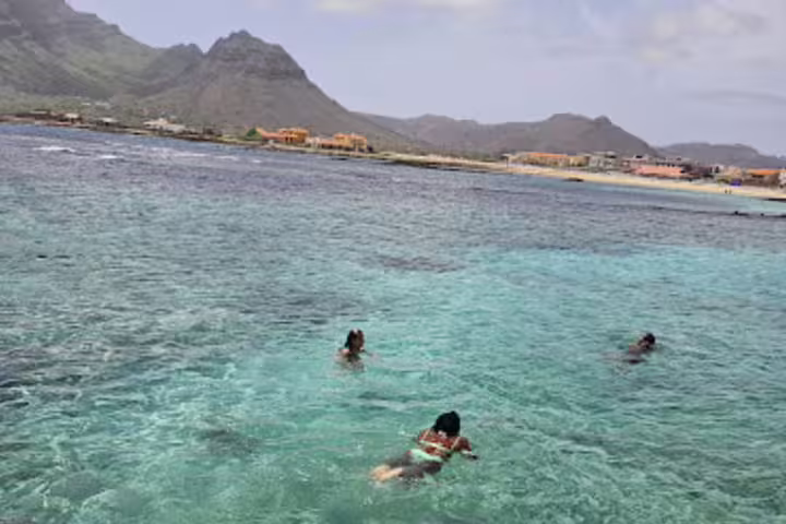Crystal-clear waters of São Vicente with swimmers enjoying the scenic backdrop of Monte Verde and charming coastal villages.