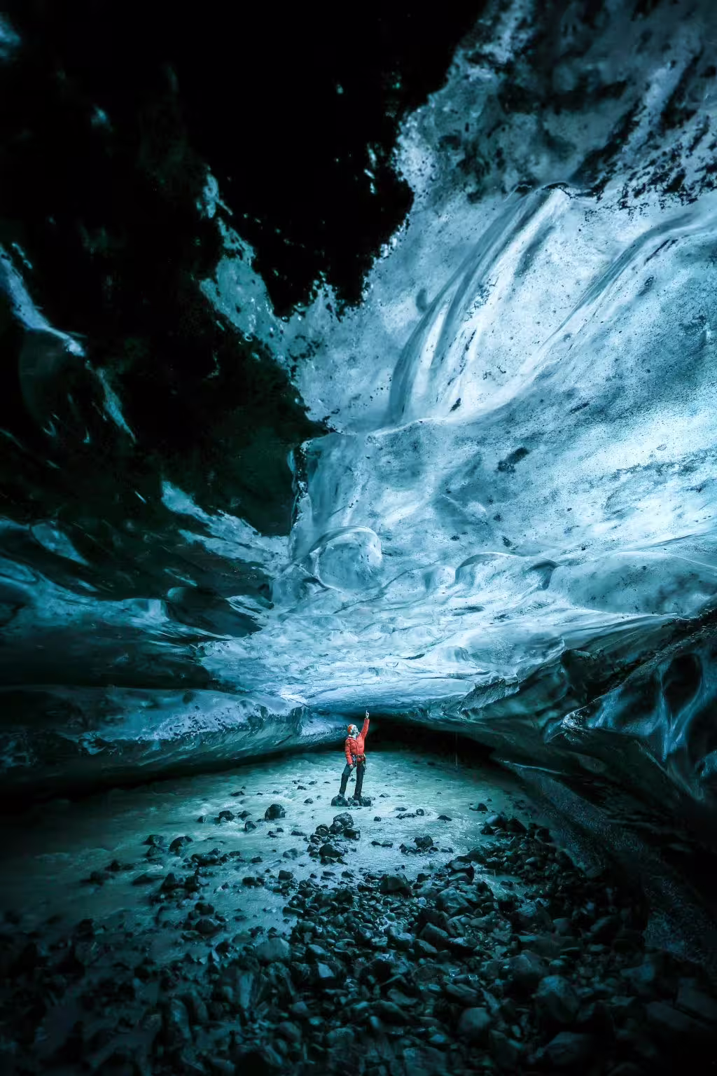 Guide in red jacket marveling at towering sapphire blue ice cave walls on an early bird glacier tour in Iceland