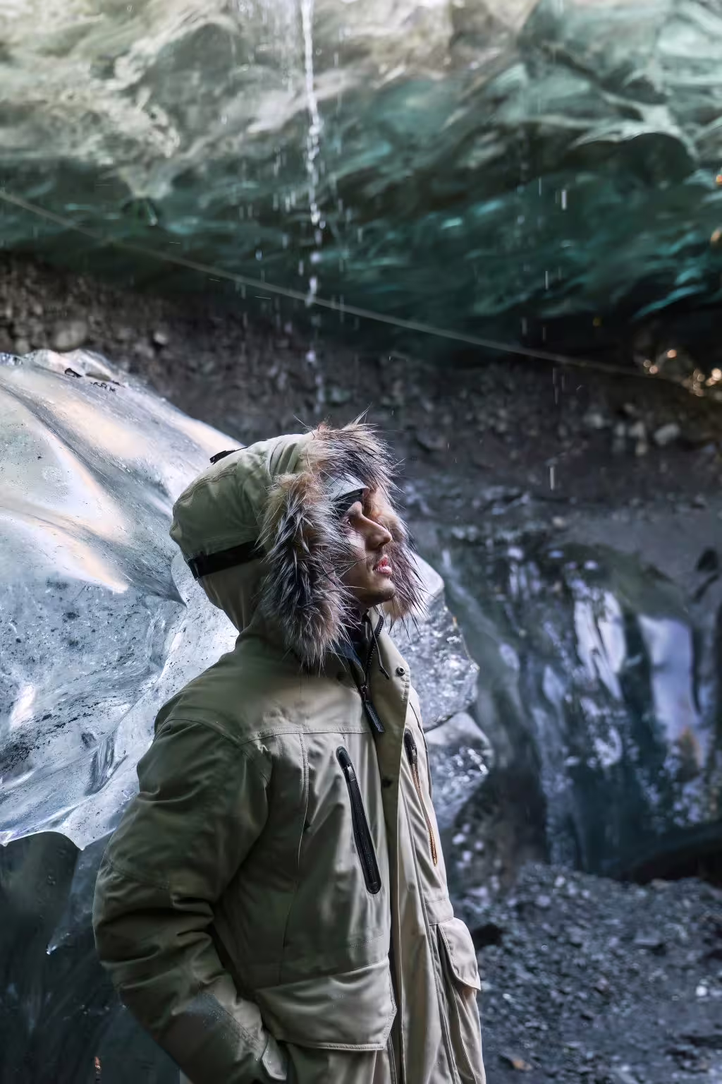 Explorer in a fur-trimmed parka gazes up at dripping sapphire ice cave walls on an early bird Iceland glacier tour