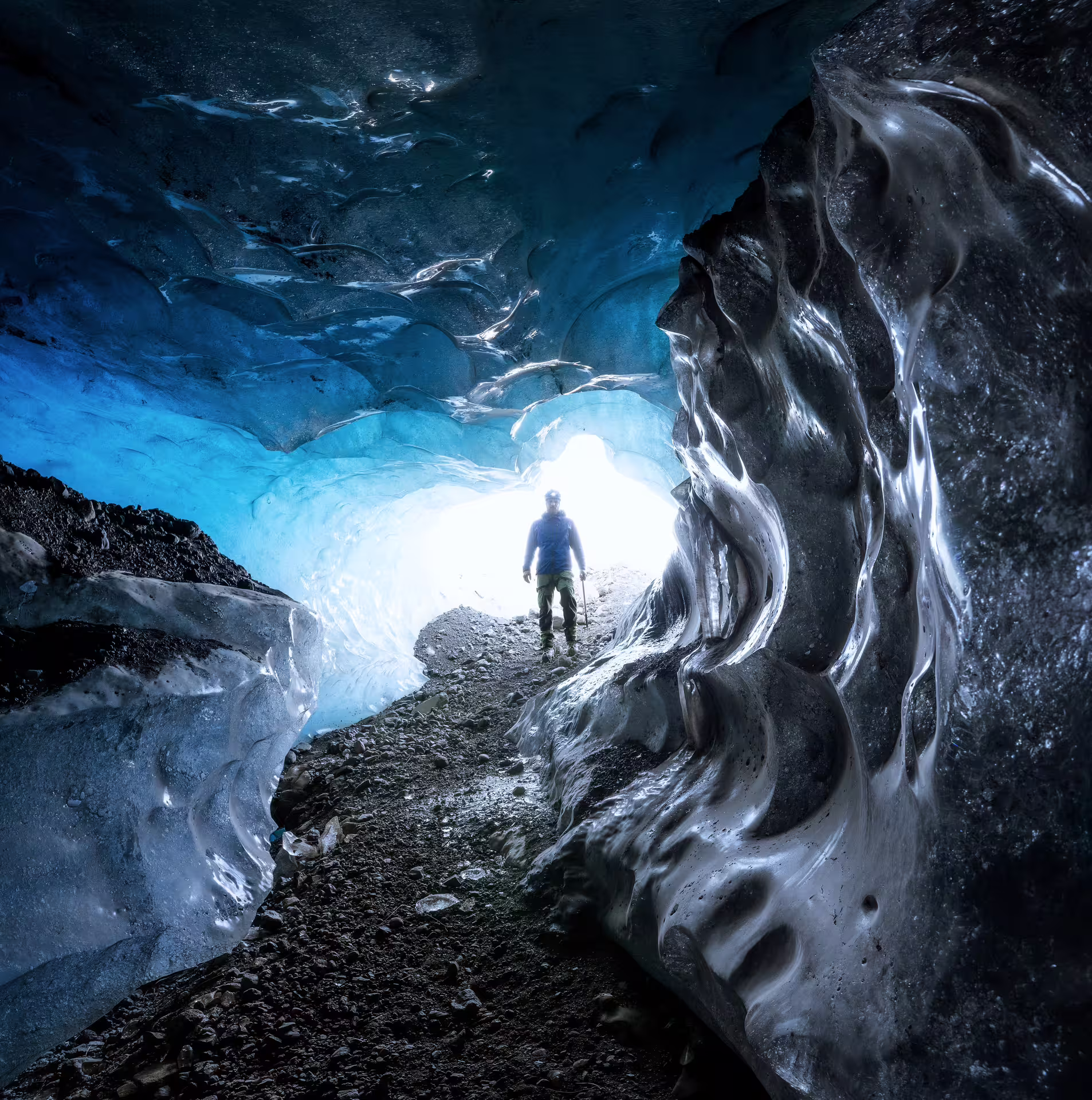 A lone explorer stands at the glowing entrance of a stunning sapphire blue ice cave in Iceland during an early bird guided tour.