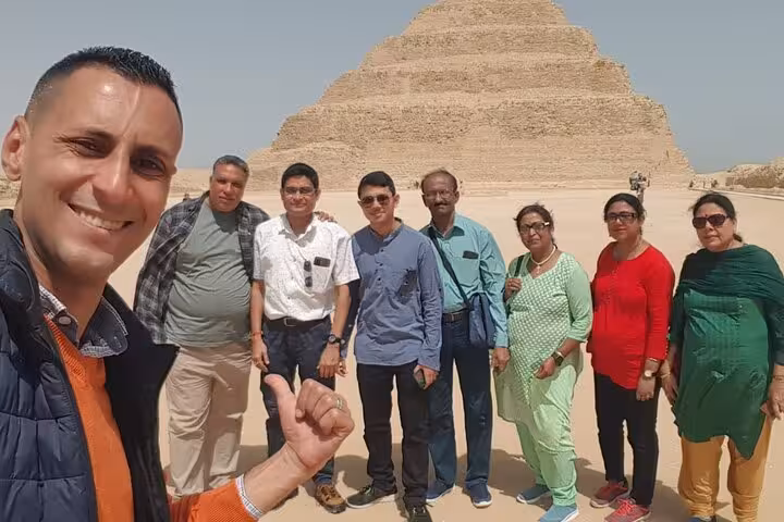 Group of tourists enjoying a guided tour at the Saqqara Pyramid site on a sunny day.