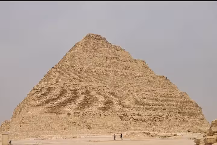 Saqqara Step Pyramid in Egypt with visitors at base, iconic sight on Saqqara & Giza Pyramids tour