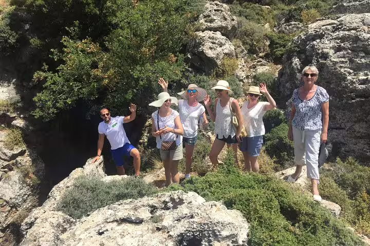 Group of tourists enjoying a sunny day hike in Sarakina Gorge, Kritza, surrounded by rugged rocks and lush greenery.