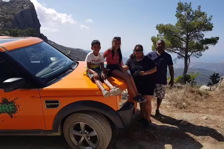 Family enjoying a scenic view from an orange SUV in the mountains near Sarakina Gorge, Kritza, on a sunny day.