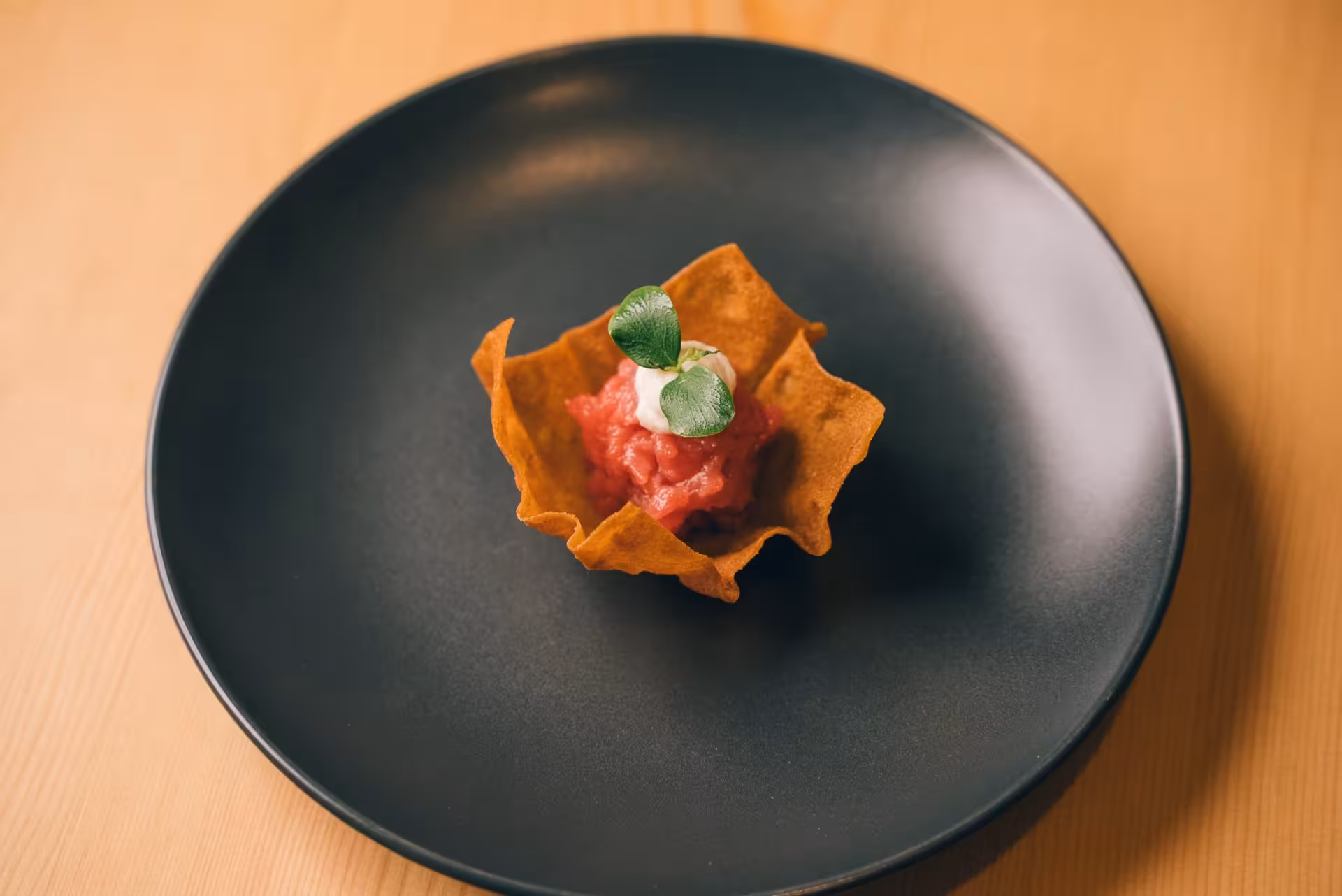 Gourmet Sardinian tapas with tartare and microgreens in a crispy shell on a sleek black plate in Olbia.