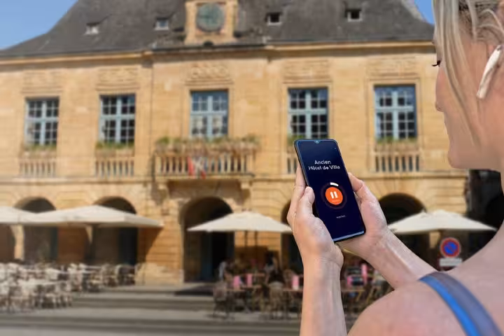 Tourist using audio guide app on smartphone in front of Ancien Hôtel de Ville in Sarlat-la-Canéda, France