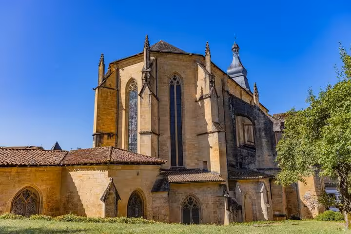 Gothic apse of Sarlat-la-Canéda cathedral with tall stained glass windows under blue sky