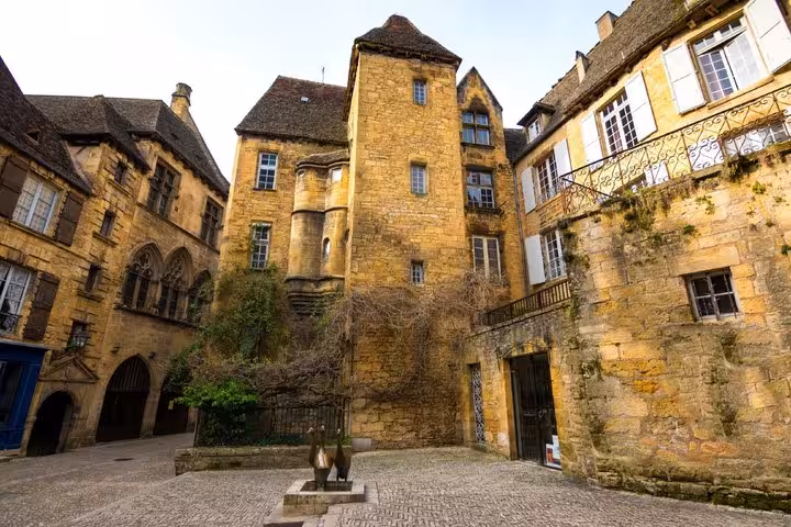 Medieval golden stone buildings surrounding a cobblestone courtyard with a small sculpture in Sarlat-la-Canéda