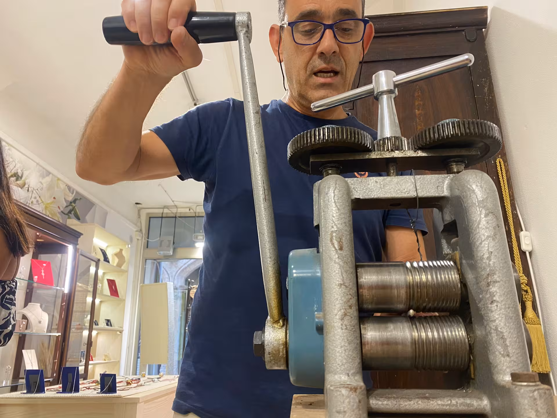 Artisan using a rolling mill in a Sassari filigree goldsmith workshop, showcasing traditional jewelry-making techniques.