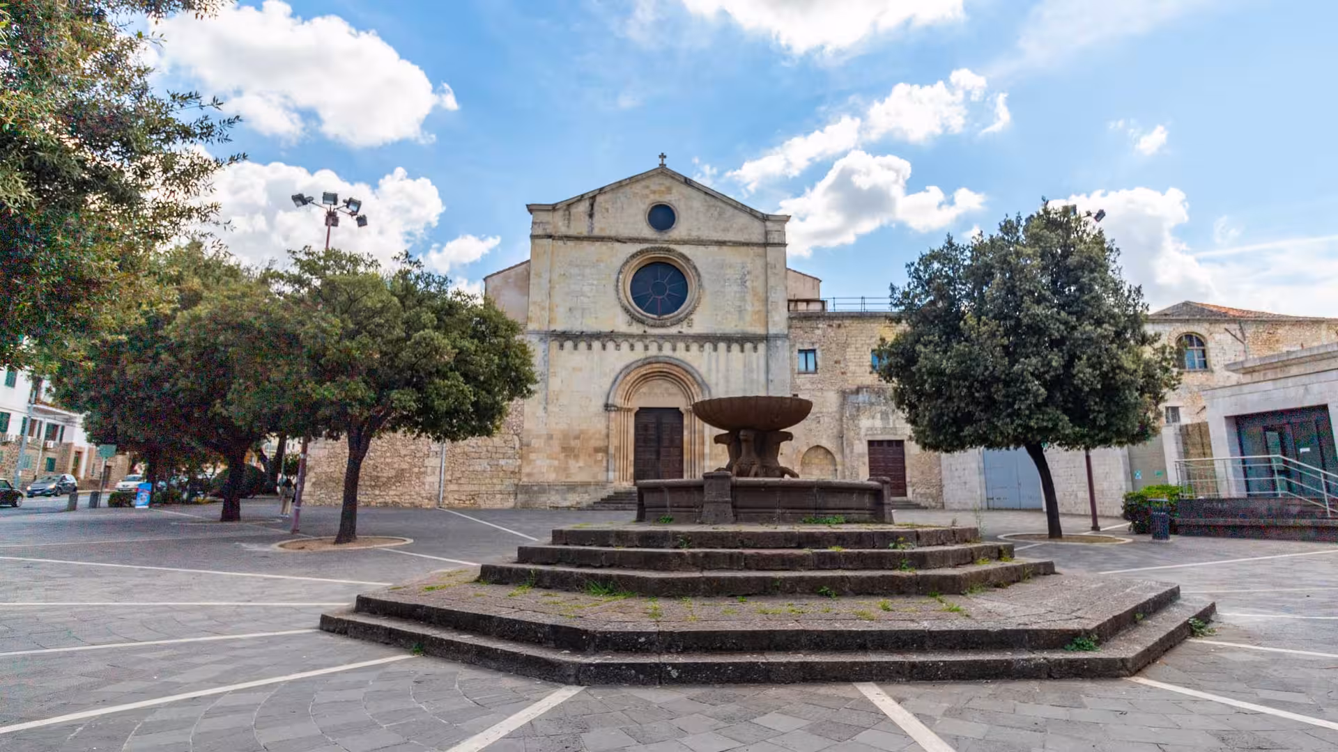 Historic church and fountain in Sassari's charming central square under a blue sky.
