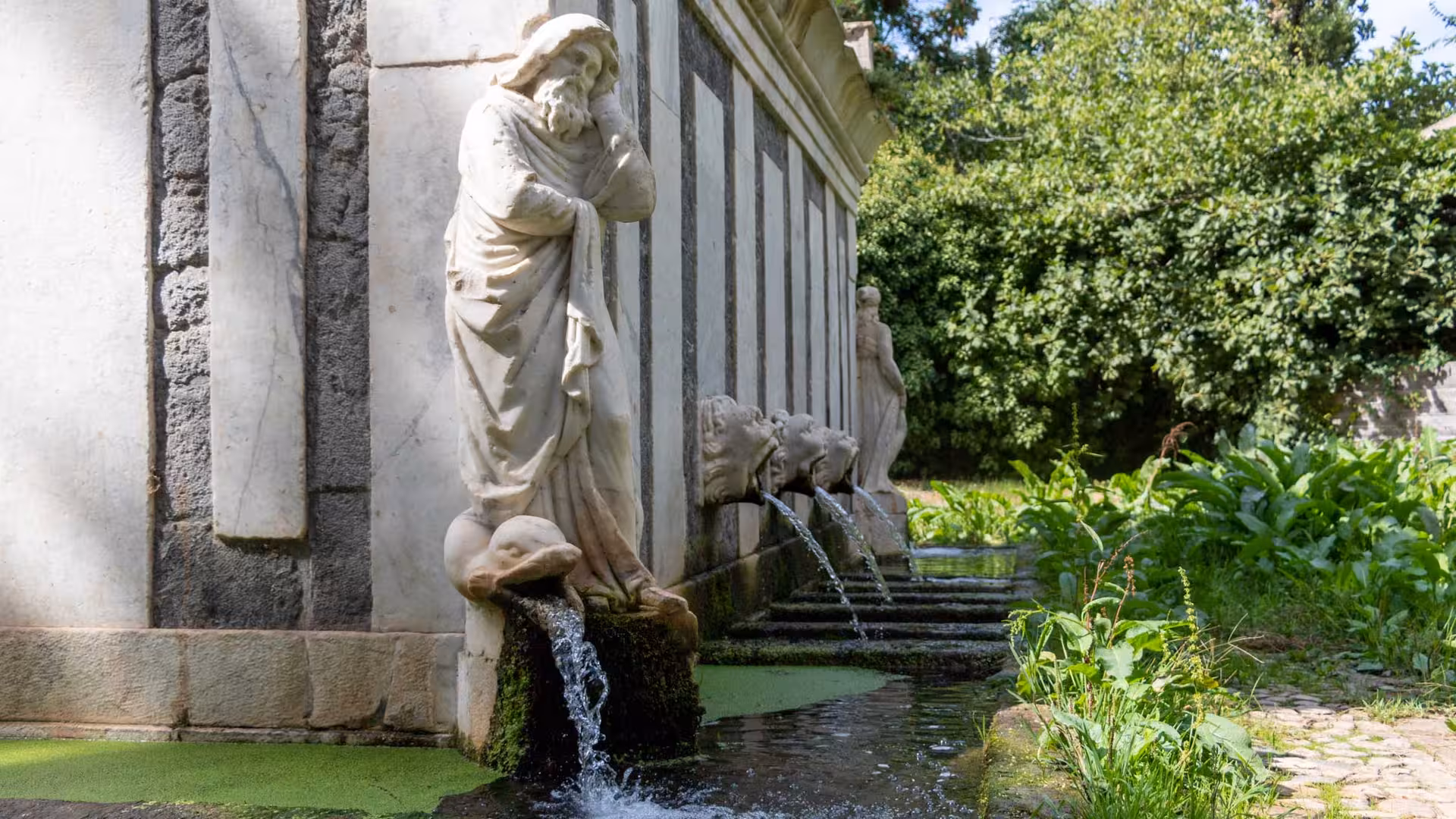 Charming statue and lion-head fountains in Sassari's old town, highlighting Renaissance artistry and lush surroundings.