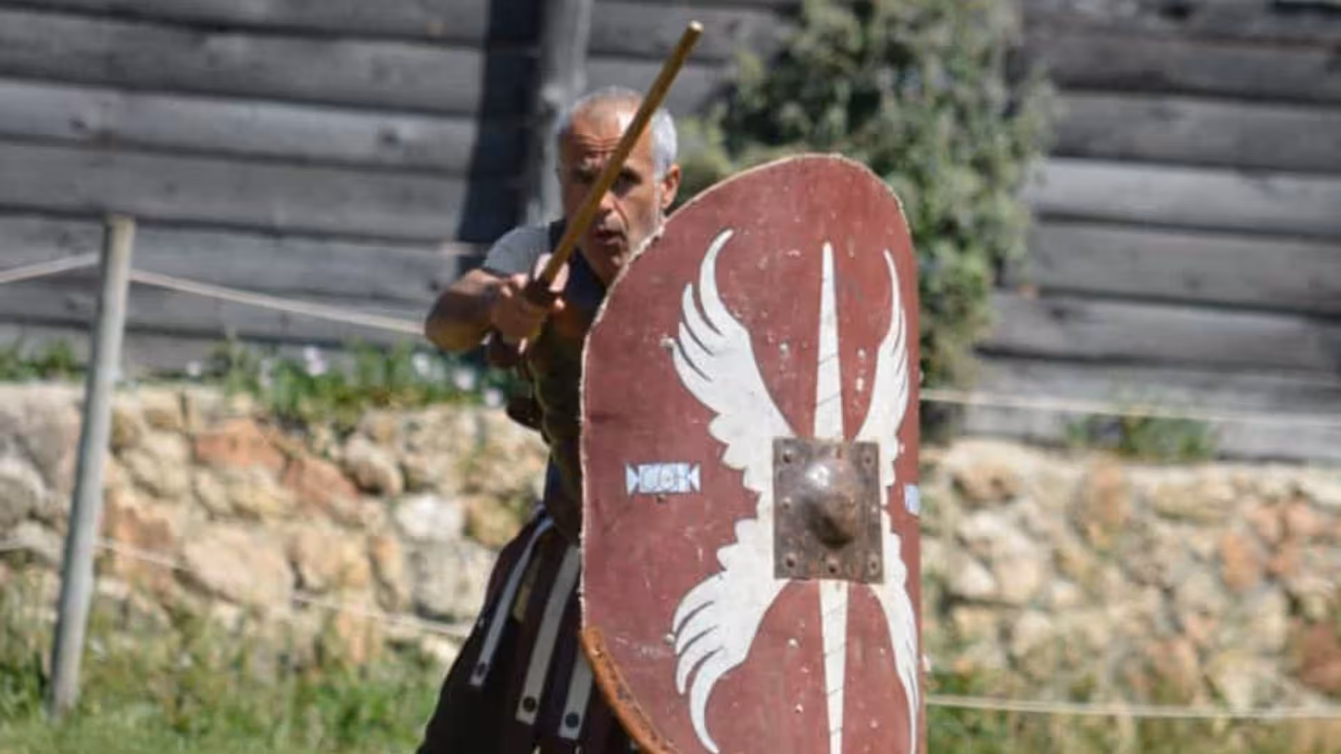 Reenactor in Roman armor with shield at Sassari's Roman Castrum, offering historical insights and cultural experiences.