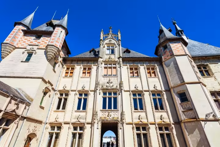 Gothic facade of Saumur Castle with ornate stone carvings, checkered towers, and arched entrance gate under blue sky