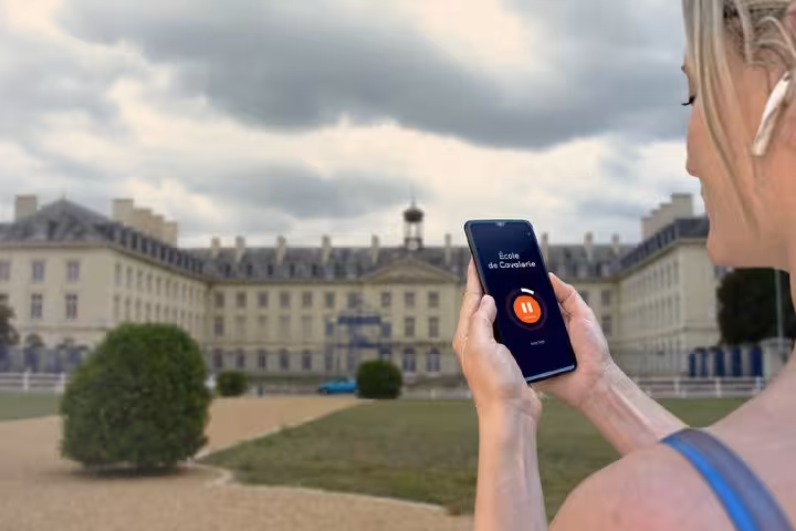 Woman holding smartphone with audio guide app in front of École de Cavalerie in Saumur, France