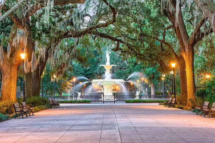 Forsyth Park fountain at dusk surrounded by Spanish moss-draped oak trees and glowing lampposts in Savannah