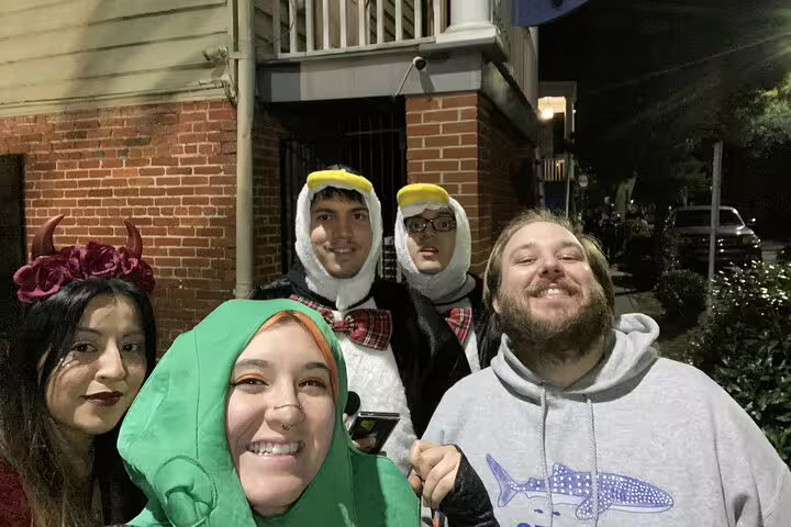 Group of friends in Halloween costumes smiling outside a brick building at night in Savannah