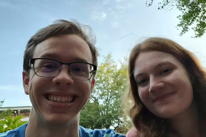 Two young people smiling outdoors during a sunny day with trees in background