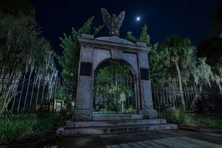 Stone archway gate with eagle sculpture at night under moonlit sky in Savannah cemetery