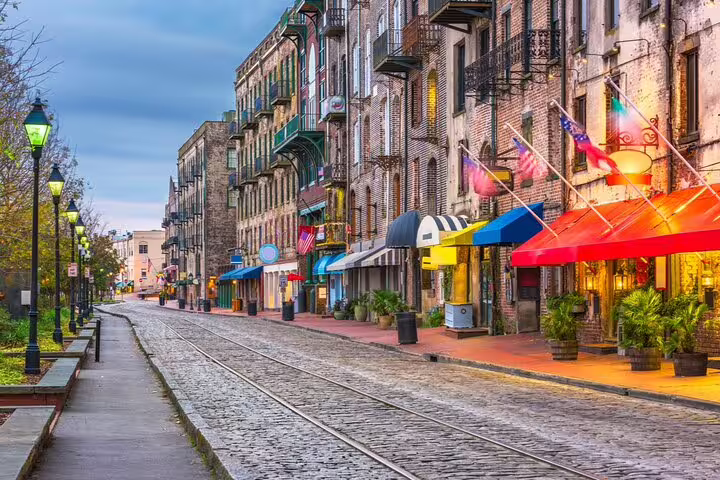 Historic cobblestone River Street in Savannah GA with colorful awnings and gas lanterns at dusk